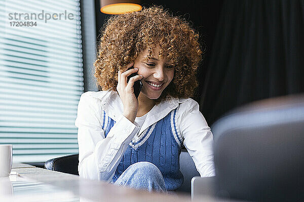 Teenager-Mädchen lächelt  während sie in einem Café mit ihrem Handy telefoniert