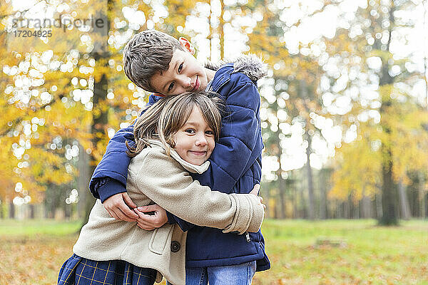 Lächelnder Bruder und lächelnde Schwester umarmen sich  während sie im Wald stehen
