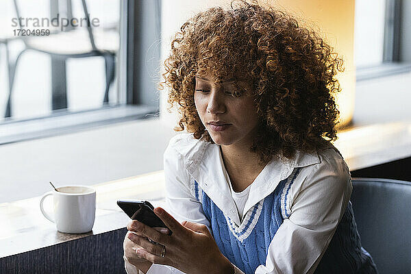 Teenager-Mädchen  das in einem Café sitzt und ein Mobiltelefon benutzt