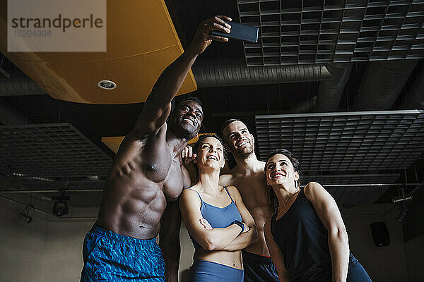 Lächelnde männliche und weibliche Athleten  die ein Selfie über ein Smartphone im Fitnessstudio machen