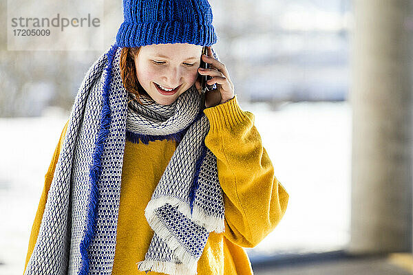 Lächelndes süßes Mädchen in warmer Kleidung  das mit einem Mobiltelefon spricht