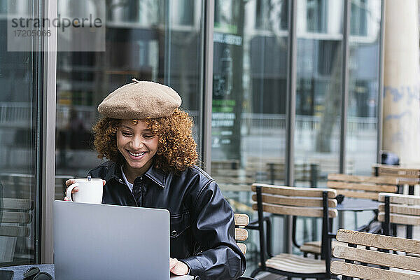 Weiblicher Teenager mit Kaffeetasse und Laptop in einem Straßencafé