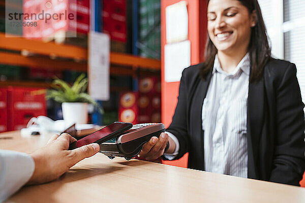 Lächelnde Managerin hält Kartenlesegerät für Kunden mit Smartphone