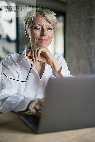 Lächelnde Unternehmerin mit Brille bei der Arbeit am Laptop im Home Office