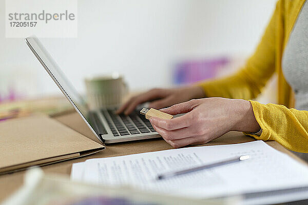 Mittlere erwachsene Frau  die einen USB-Stick neben einem Laptop auf einem Tisch zu Hause hält