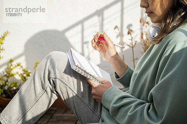 Frau schreibt in ein Buch  während sie auf dem Balkon sitzt