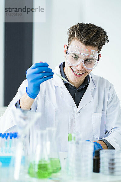 Lächelnder männlicher Wissenschaftler  der bei der Arbeit im Labor eine Pipette hält