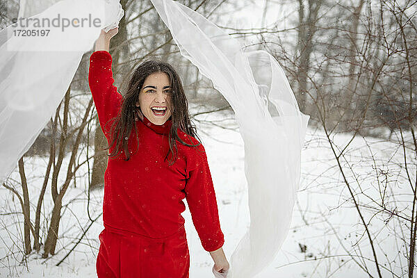 Fröhliche Frau spielt mit Tuch auf schneebedecktem Land