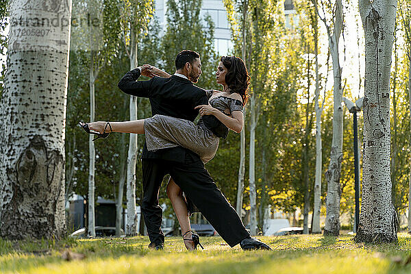 Männlicher Tänzer hebt Frau beim Tangotanzen im öffentlichen Park im Sommer