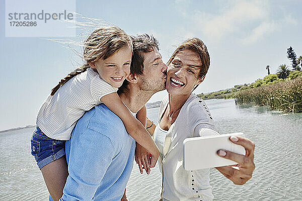 Fröhliche Familie nimmt Selfie durch Handy am See