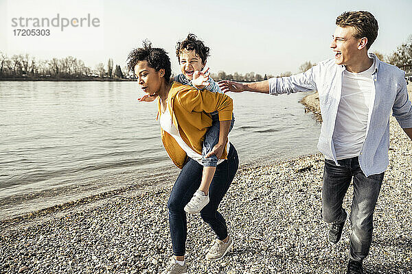 Mutter nimmt fröhlichen Jungen beim Laufen am Seeufer huckepack