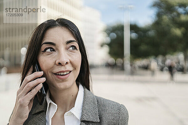 Nachdenkliche Geschäftsfrau  die in der Stadt mit einem Smartphone telefoniert
