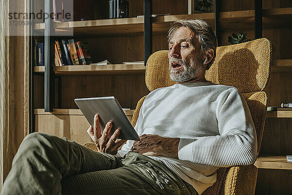 Mann spricht über Videokonferenz durch digitale Tablette  während er zu Hause sitzt