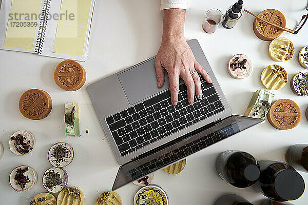 Die Hand einer Unternehmerin tippt auf einem Laptop über dem Tisch