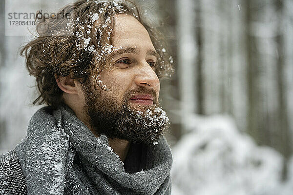 Lächelnder Mann mit schneebedecktem Haar und Bart  der im Wald steht und wegschaut