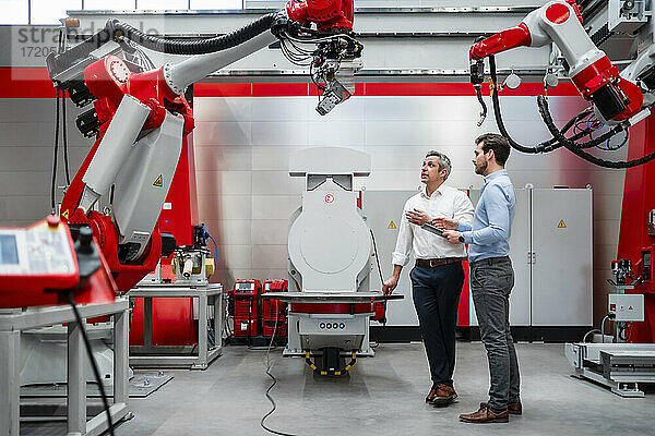 Älterer männlicher Unternehmer erklärt einem Kollegen in einer Fabrik einen Roboterarm