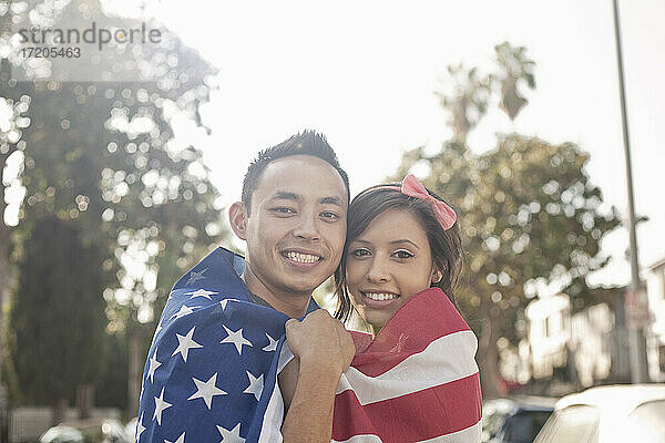 Lächelndes Paar  das in eine amerikanische Flagge eingewickelt im Freien steht