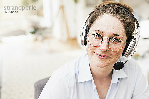 Lächelnde weibliche Fachkraft mit Brille und drahtlosen Kopfhörern