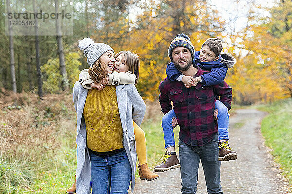 Eltern nehmen ihre Kinder beim Herbstspaziergang im Wald huckepack