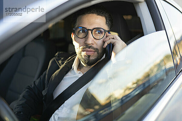 Gutaussehender Geschäftsmann schaut weg  während er im Auto mit seinem Handy telefoniert