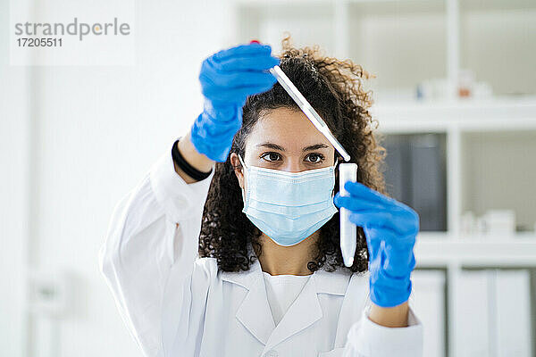 Junge Ärztin testet Lösung in einem Röhrchen im Chemielabor während einer Pandemie