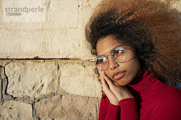 Afro-Frau mit Sonnenbrille und Händen am Kinn schaut weg