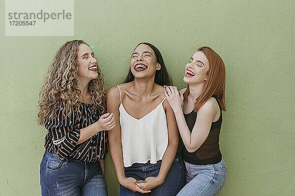 Multiethnische Freundinnen lachend vor grüner Wand