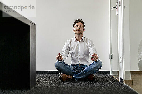 Männlicher Unternehmer meditiert Yoga im Büro an der Wand