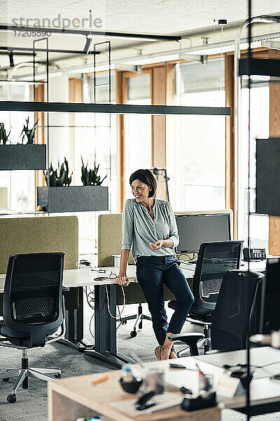 Unternehmerin lehnt sich im Büro an den Schreibtisch