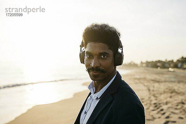 Afro-Mann mit Kopfhörern am Strand an einem sonnigen Tag