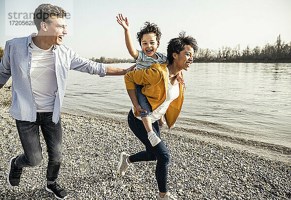 Fröhliche Familie hat Spaß beim Laufen am Seeufer an einem sonnigen Tag