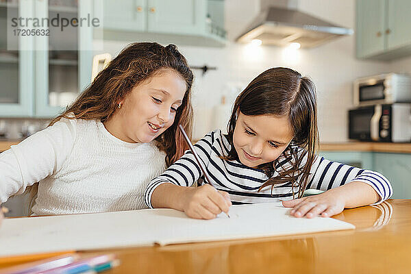 Mädchen zeichnet auf Papier  während sie mit ihrer Schwester am Esstisch in der Küche sitzt