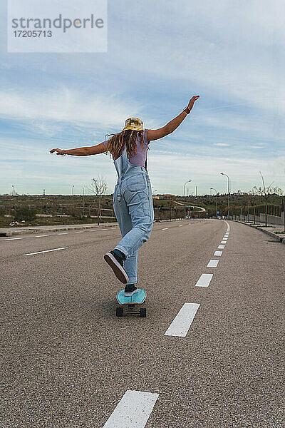 Frau in Latzhose beim Skaten mit Skateboard auf der Straße