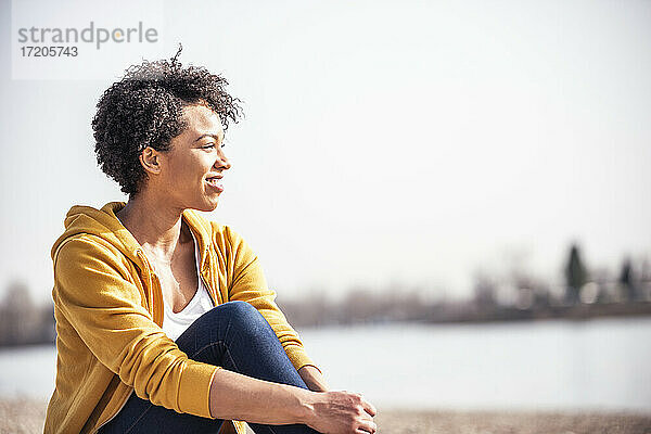 Lächelnde Frau sitzt im Freien an einem sonnigen Tag