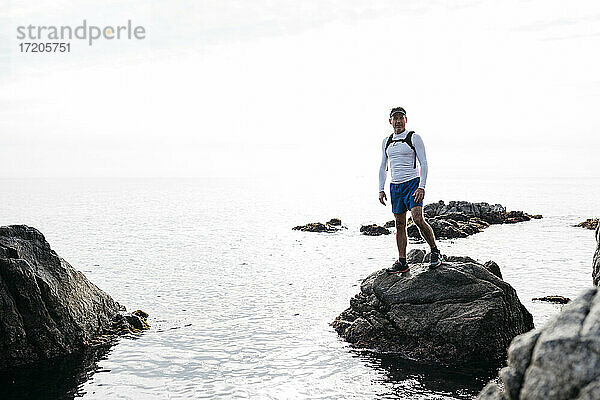 Älterer Mann steht auf einem Felsen inmitten des Meeres vor klarem Himmel