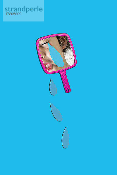 Reflexion des Mädchens auf Handspiegel mit Tränen über blauem Hintergrund