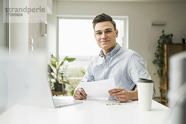 Junger männlicher Unternehmer mit Dokument im Home Office sitzend