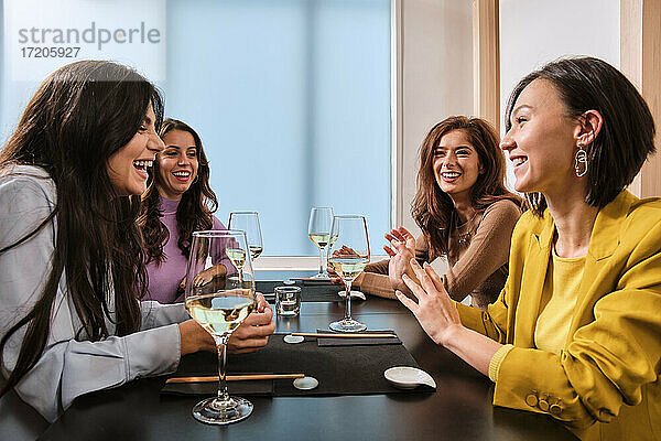 Weibliche Freunde mit Weingläsern  die lachend am Tisch im Restaurant sitzen