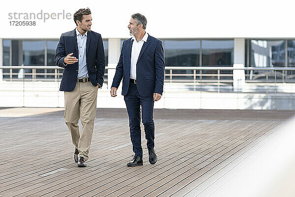 Männlicher Unternehmer im Gespräch mit einem Kollegen beim Spaziergang auf der Terrasse eines Bürogebäudes