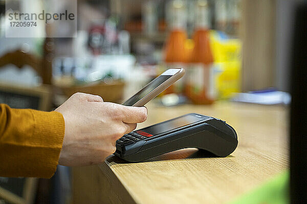 Frau benutzt Smartphone zum kontaktlosen Bezahlen an der Kasse eines Lebensmittelgeschäfts