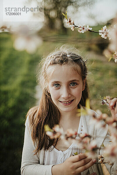 Nettes Mädchen lächelt  während es neben Mandelbaumblüten steht