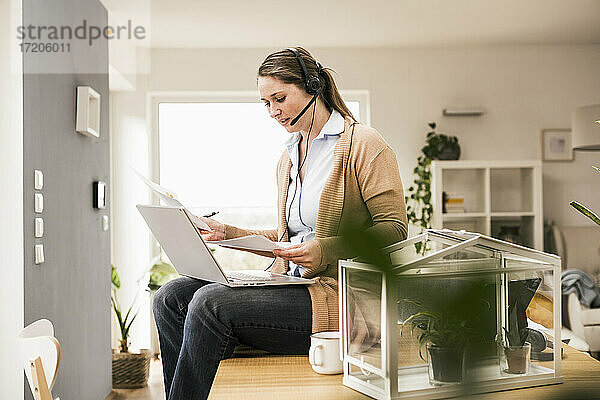 Weibliche Fachkraft prüft ein Dokument  während sie zu Hause am Laptop sitzt