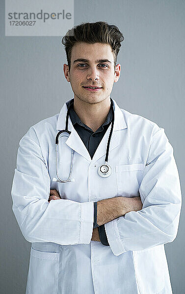 Männlicher gut aussehender Arzt mit verschränkten Armen vor einer grauen Wand