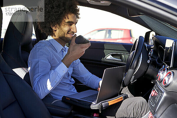 Männlicher Berufstätiger  der ein Smartphone hält und einen Laptop im Auto benutzt