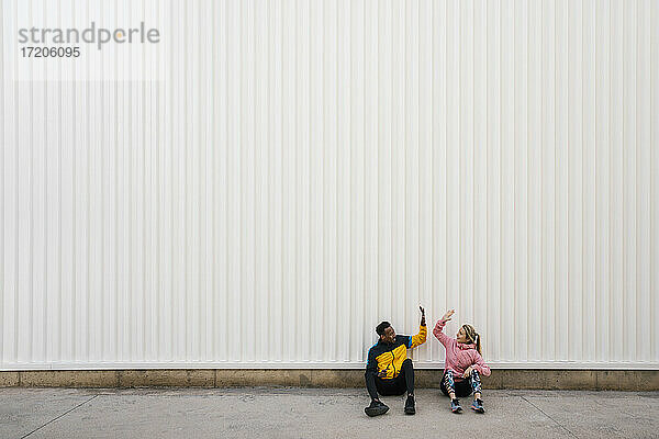 Mann und Frau machen High-Five  während sie auf dem Boden vor der Wand sitzen