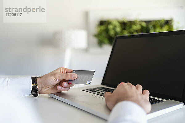 Geschäftsmann  der eine Kreditkarte hält  während er einen Laptop im Büro benutzt
