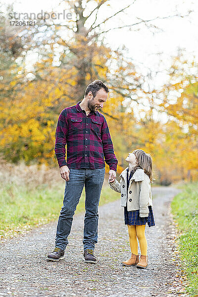 Lächelnder Vater  der seine Tochter anschaut  während er im Wald steht und die Hände hält