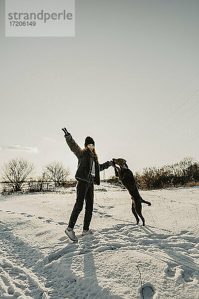Teenager-Mädchen spielt mit Hund im Schnee in der Winterdämmerung