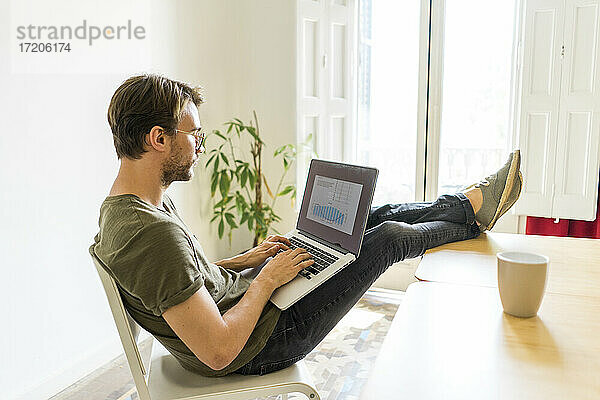 Junger männlicher Unternehmer arbeitet am Laptop und legt die Füße auf den Tisch im Büro