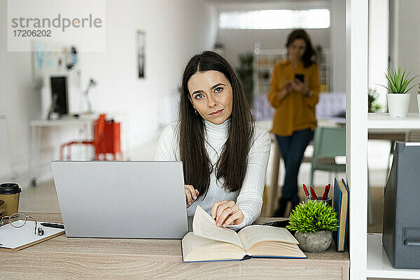 Junge Frau mit Laptop sitzt am Tisch im Wohnzimmer